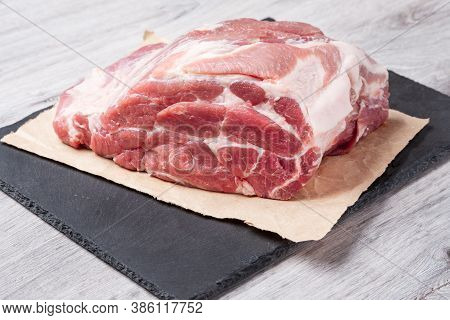 A Piece Of Uncooked Meat Of Pork Neck On Black Stome Plate On Gray Table. Close Up View.