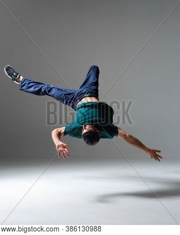 Stylish Young Guy Breakdancer Jumps Dancing Hip-hop Isolated On Gray Background. Breakdance Lessons