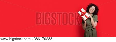 Cute Brunette Woman With Curly Hair Is Holding A Present In A Packed Box And Smile At Camera Near Re