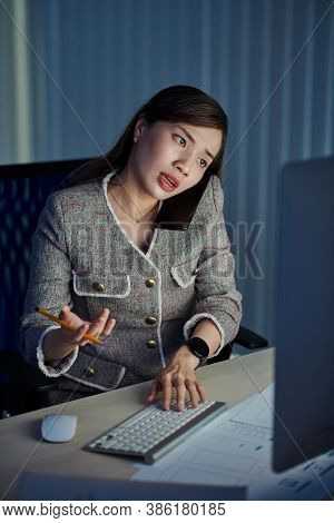 Young Asian Female Ui Designer Working In Dark Office Late At Night, Answering Phone Call From Clien