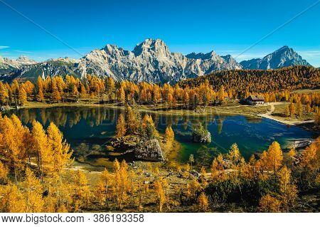 Beautiful Colorful Autumn Forest With Majestic Alpine Lake. Colorful Larches And Small Cute House On