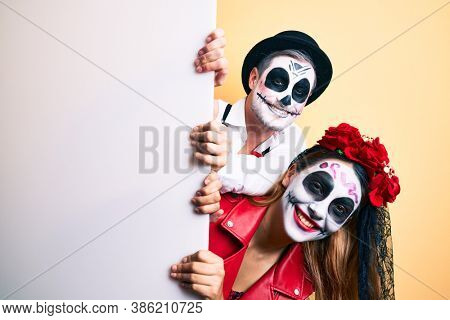 Couple wearing day of the dead costume holding blank empty banner looking positive and happy standing and smiling with a confident smile showing teeth 