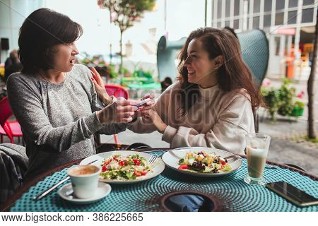 Mature Mother And Her Young Daughter Sit Together In Cafe Or Restaurant. Shocked Mature Woman Hearin