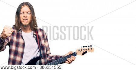 Handsome caucasian man with long hair playing electric guitar annoyed and frustrated shouting with anger, yelling crazy with anger and hand raised 