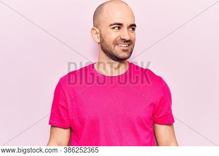 Young handsome bald man wearing casual t shirt looking to side, relax profile pose with natural face and confident smile. 