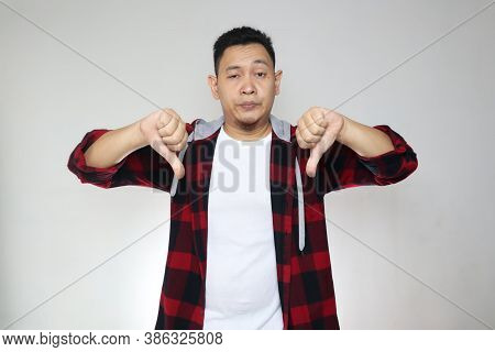 Portrait Young Asian Man Wearing Casual Shirt Shows Upset Expression With Thumbs Down, Over White Ba
