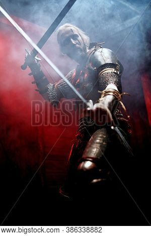 Fantasy medieval knight in armor is fighting with  two swords in his hands. The Witcher man.