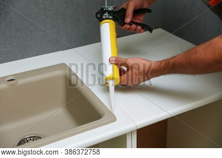 Worker Seals Kitchen Sink With Sealant. Hands Of Worker Works With Construction Sealant Gun In The K