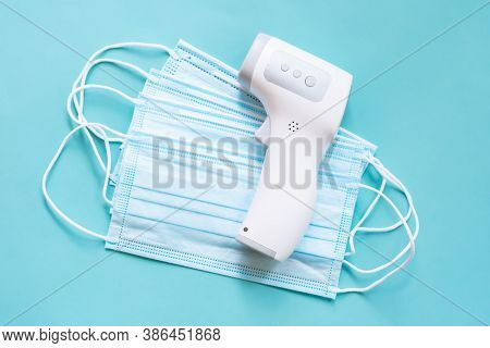 Digital Infrared Thermometer Is Lyiing On Stack Of Medical Masks On Blue Background. Health Protecti