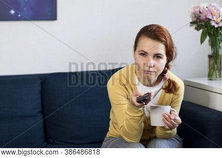 Bored Lonely Young Woman Sitting On Sofa In Living Room, Watching Tv, Switching Channels With Tv Rem