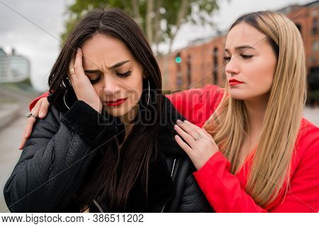 Portrait Of A Young Woman Consoling And Comforting Her Upset Friend While Sitting Outdoors At The St