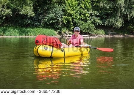 Mature man fishing from the packraft yellow boat on the river at summer time