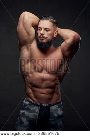 Brutal Military Athlete With Naked Torso And With Beard And Mustache Posing In Dark Gray Background.