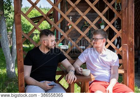 Two Handsome Guys Sitting On Back Yard Of Coutry House, Male Friends Resting Outdoors, Talking And L