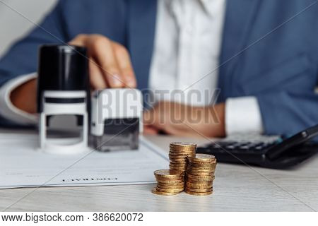 Businessman Approves Contract. Stack Of Coins, Contract And Stamps On Desk. Business And Money Conce