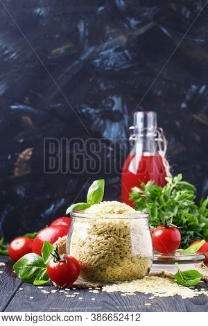 Italian Uncooked Pasta Riso Or Orzo In A Glass Jar, Tomatoes And Green Basil, Black Background, Sele
