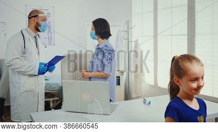 Parent And Doctor Talking In Madical Office Wearing Protective Mask During Covid-19 Pandemic. Physic