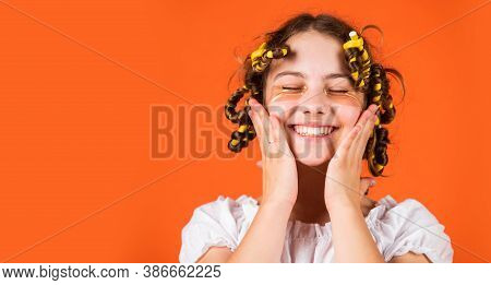 Styling Tips. Teen Hobbies. Small Girl Curling Hair Using Curlers Orange Background. Hairdresser Sal