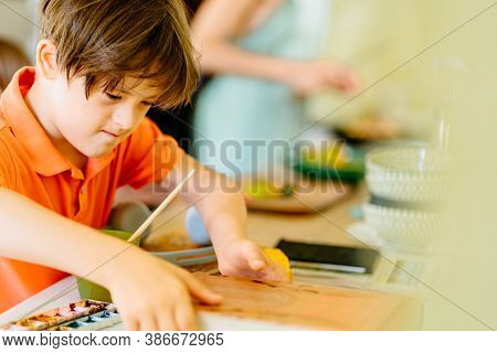 Child Boy With Down Syndrome Wears Orange T-shirt Taking Book Or Sketchbook At Home.