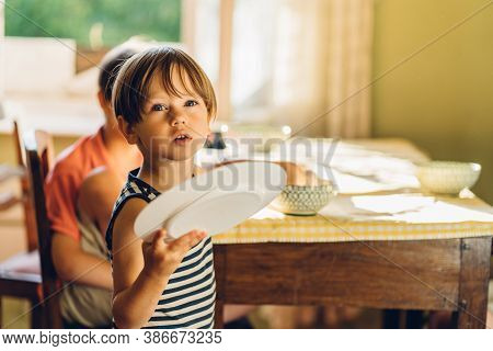 Cute Little Preschooler Boy In Striped T-shirt Help His Mother At Kitchen In Home. Child Holding Dis