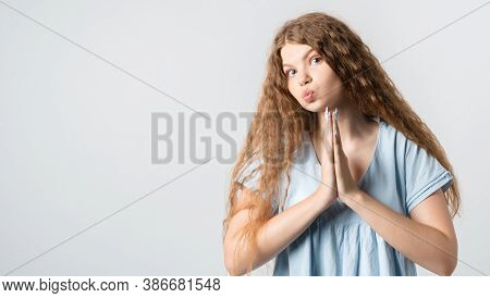 Please, Help Me. Emotive Pleased European Girl With Curly Long Hair, Keeps Hands In Praying Gesture,