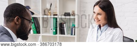 Horizontal Image Of Joyful Doctor Looking At African American Patient In Hospital, Panoramic Shot