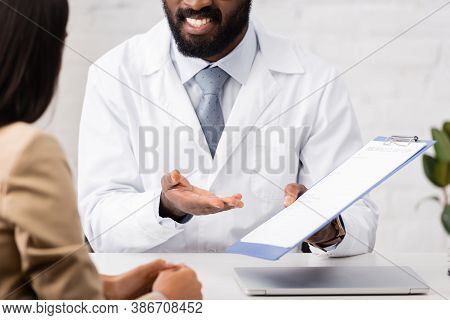 Cropped View Of African American Doctor Pointing With Finger At Clipboard With Insurance Form Near P