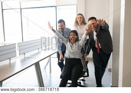 Playful Business Group Push Female Colleague Sitting In Chair And Having Fun In Office