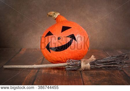 One Halloween Pumpkin And A Witchs Broom On A Brown Background.