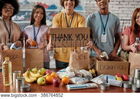 Cropped Shot Of Group Of Diverse Young Volunteers Packing Food And Drinks Donation, Guy Holding Card