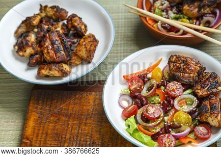 Plates Of Pan-asian Sesame Salad And Grilled Chicken Pieces In Terriyaki Sauce.