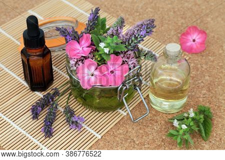 Naturopathic herbal medicine with summer flowers and herbs loose and steeping in a jar with oils to make aromatherapy essential oil. Still life on bamboo and cork. Natural health care concept.