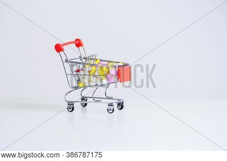 Small Grocery Cart With A Bunch Of White, Pink And Yellow Pills,isolated On Yellow Background. Purch