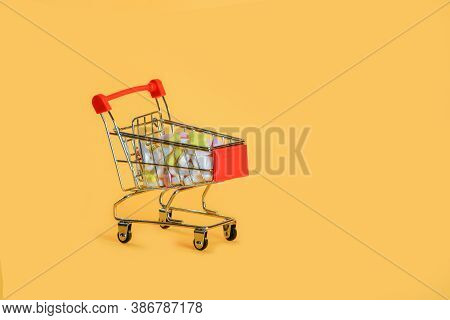 Small grocery cart with a bunch of white, pink and yellow pills,isolated on yellow background.Pharmaceutical business.Sell treatment.