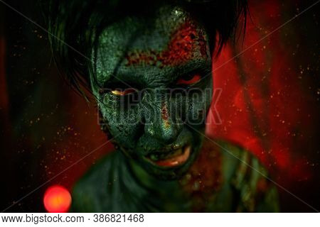 Halloween, horror movie. Close-up portrait of a scary zombie boy teenager in geen and red light. 