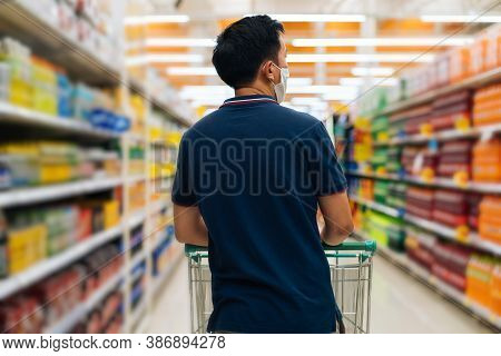 Rear View Young Adult Asian Man Wearing A Face Mask While Shopping With Cart Trolley In Grocery Supe