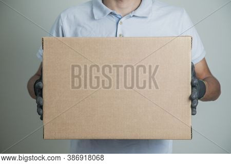 Detail Of Man With Black Gloves Holding A Cardboard Box For Delivering Products On Gray Background. 