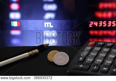 Heap Of Italy Coins With Calculator And Pencil On Black Floor With Digital Board Of Currency Exchang