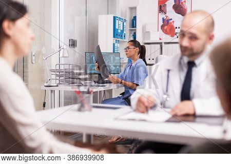 Nurse Checking Patient X-ray In Hospital Office While Doctor Is Explaining Medical Diagnosis To Hand