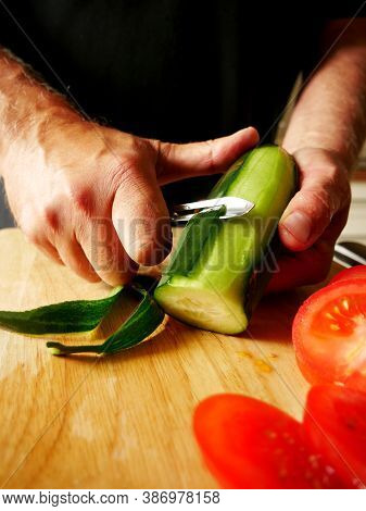 Man Peeling A Cucumber On A Wooden Board.