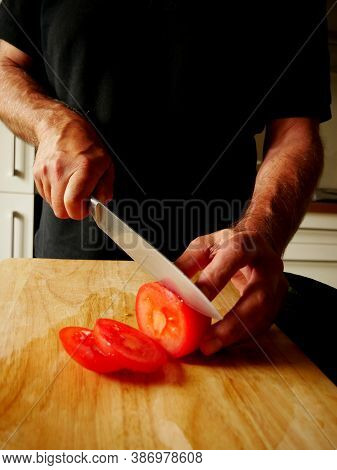 Man Cutting Tomatoes On A Wooden Board