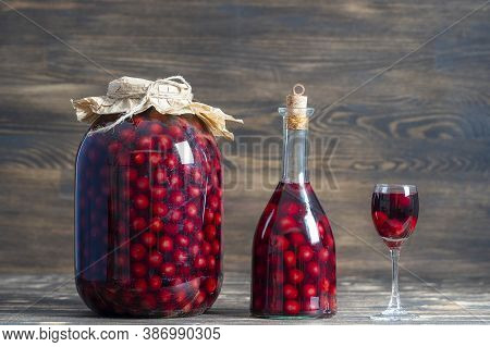 Homemade Tincture Of Red Cherry In A Glass Bottle, Jar And A Wineglass On Wooden Background, Ukraine