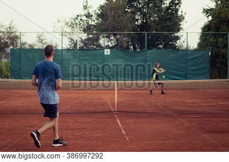 Man In Blue Shirt And Blue Pants Seen From Behind Playing Tennis, Wide Open Clay Orange Playing Fiel