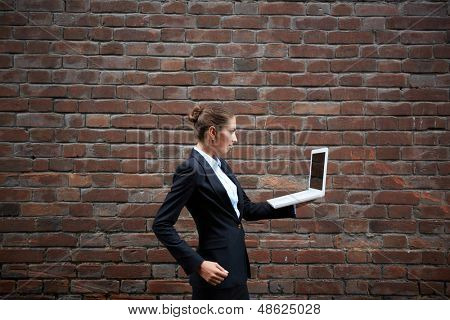 Billede af alvorlige forretningskvinde med laptop gåture langs mur