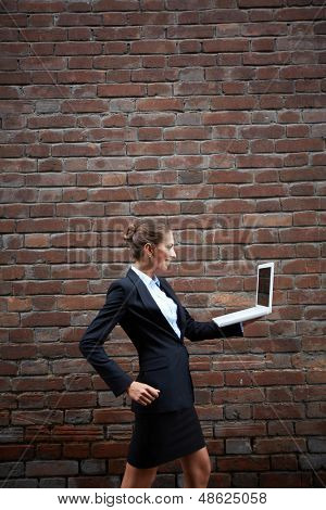 Billede af elegante forretningskvinde med laptop gåture langs mur