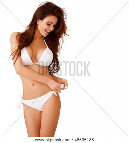 Laughing sexy busty young brunette woman in a white bikini playing with the bow on her hip  three quarter isolated studio portrait