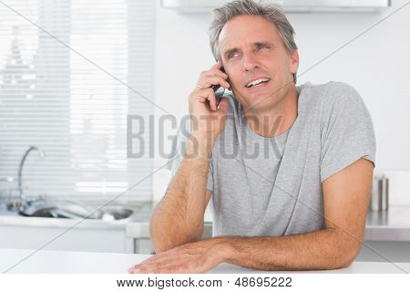 Šťastný člověk, že telefonní hovor v kuchyni sedí u pultu