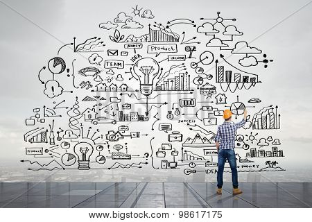 Back view of man engineer drawing plan sketches on wall
