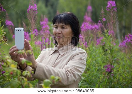 Senior Chuvash woman taking pictures by phone in park