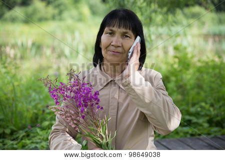 Senior Chuvash woman speaking by phone on summer green background